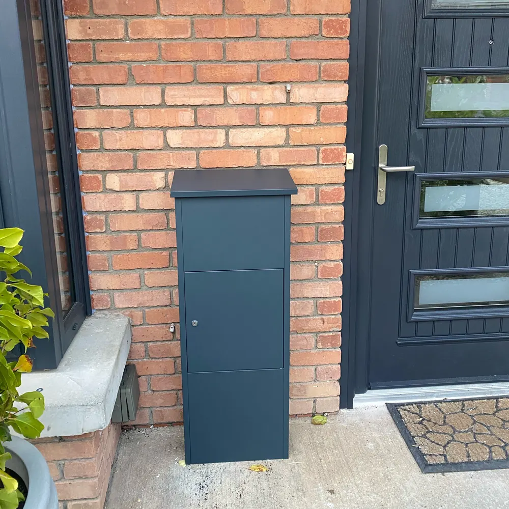 Outdoor parcel box Goldcrest positioned by a dark grey front door, customer-supplied photo